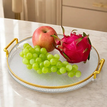 Bandeja decorativa redonda con asas doradas y superficie transparente para servir frutas